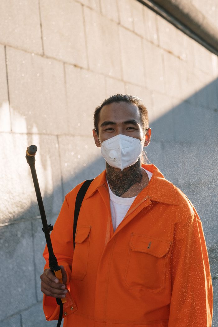 our-story Man wearing protective coveralls and face mask spraying outdoors.