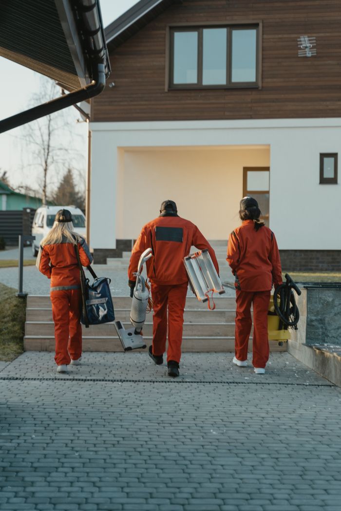 who-we-are Cleaning crew in red uniforms with equipment approaching a modern house exterior.